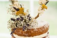 a naked wedding cake decorated with dried flowers, leaves and fresh blooms in yellow and white for a rustic wedding