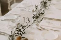 a neutral minimalist wedding tablescape with a greenery runner, all crispy white around and white menus is a cool idea