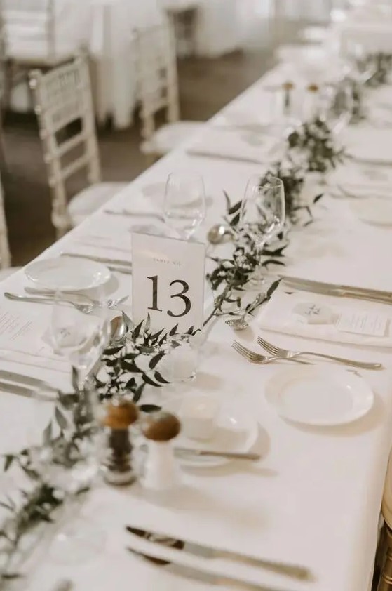 a neutral minimalist wedding tablescape with a greenery runner, all crispy white around and white menus is a cool idea