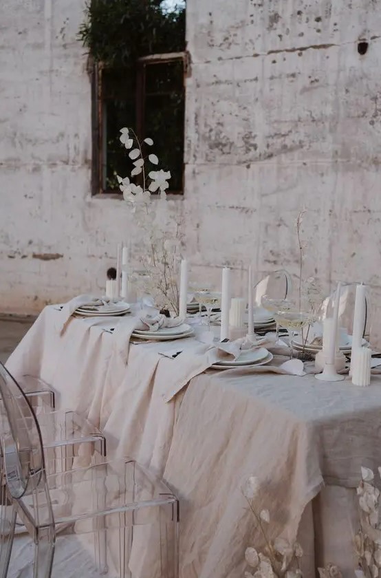 a neutral winter wedding table setting with textural linens, pillar candles, lunaria centerpieces and simple white porcelain