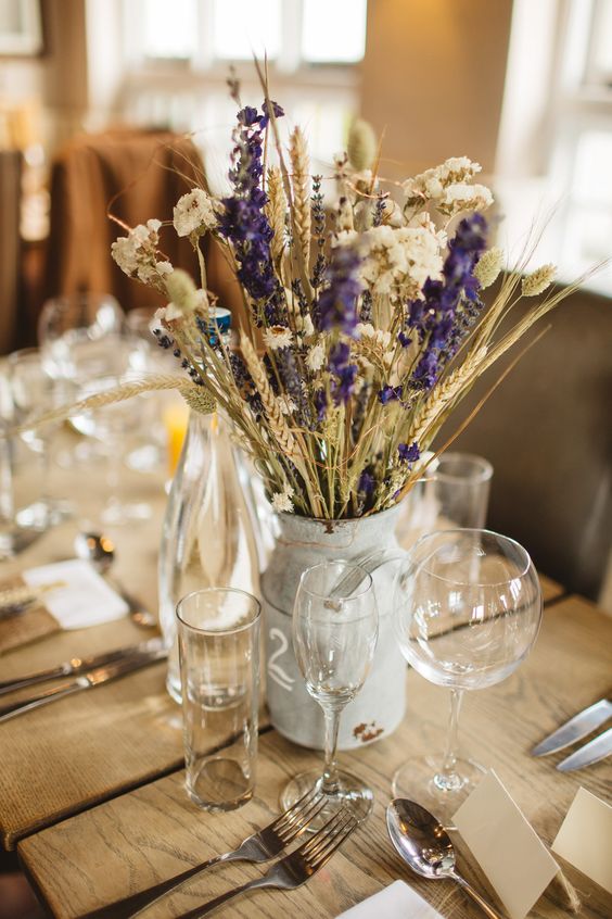a rustic wedding centerpiece with wheat, dried blooms and fresh purple ones for a touch of color