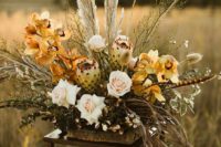 a sculptural boho wedding centerpiece with yellow orchids, ivory roses, dried foliage and pampas grass in earthy tones