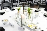 a stylish minimalist wedding tablescape with candle lanterns with blooms and a candle, with black napkins and a white tablecloth