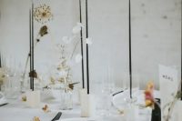 a stylish minimalist wedding tablescape with white plates and linens, white candleholders, tall and thin black candles and dried and fresh blooms
