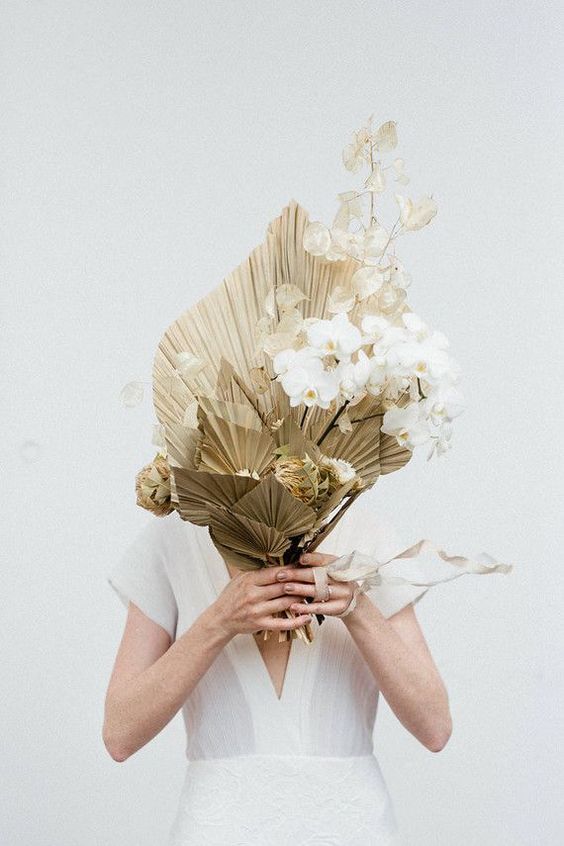 a unique wedding bouquet of gilded leaves, lunaria and white orchids features a very unusual structure