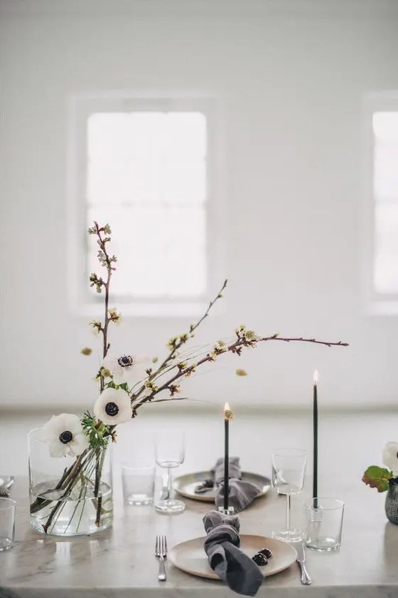 an elegant minimalist wedding table setting with neutral plates, grey napkins, white blooms, thin and tall black candles
