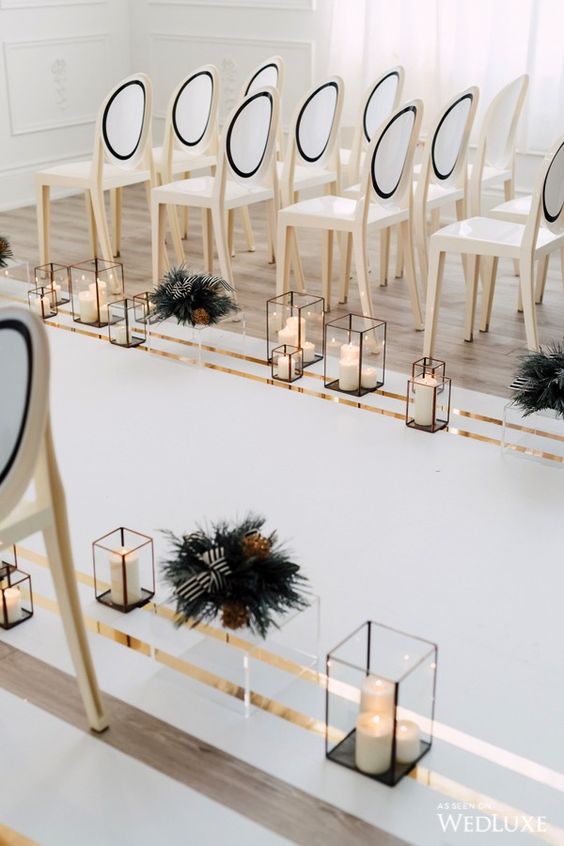 a modern luxurious wedding aisle with candle lanterns, dark foliage and elegant white and black chairs