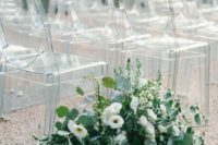12 ghost chairs and a wooden planter with lush greenery and white blooms make up a gorgeous minimal wedding aisle
