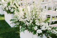 14 white chairs and white planters with greenery and white blooms make up a chic and stylish modern wedding aisle