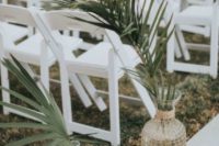 20 a modern tropical wedding aisle with white chairs and palm leaves in clear and wicker vases for a stylish and simple look