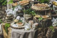 23 a dessert table perfectly styled for the theme with tree stumps and wood slices, pies and tarts in cloches and lots of greenery and moss