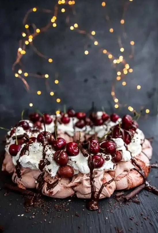 a blush pavlova wreath topped with whipped cream, chocolate drip, chocolate sticks and cherries is a lovely idea for a summer or fall wedding