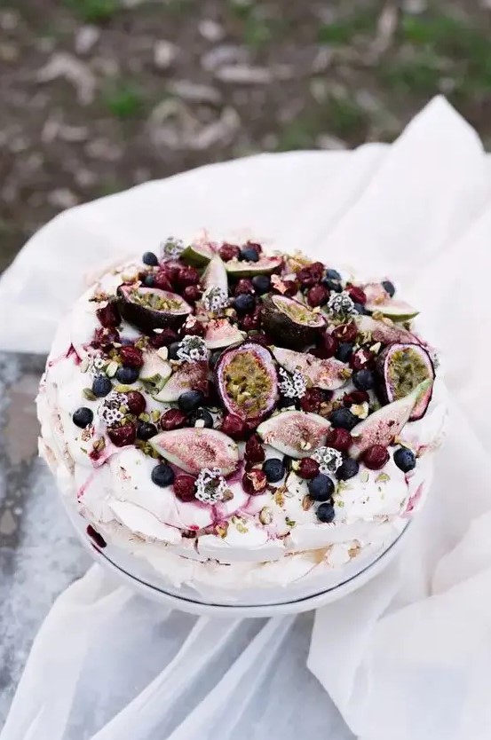 a catchy pavlova wedding cake topped with fresh fruits and berries, some blooms and nuts is fantastic