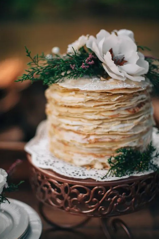 a chic and simple crepe wedding cake with sugar powder, greenery and white blooms on top is a great idea for a woodland wedding