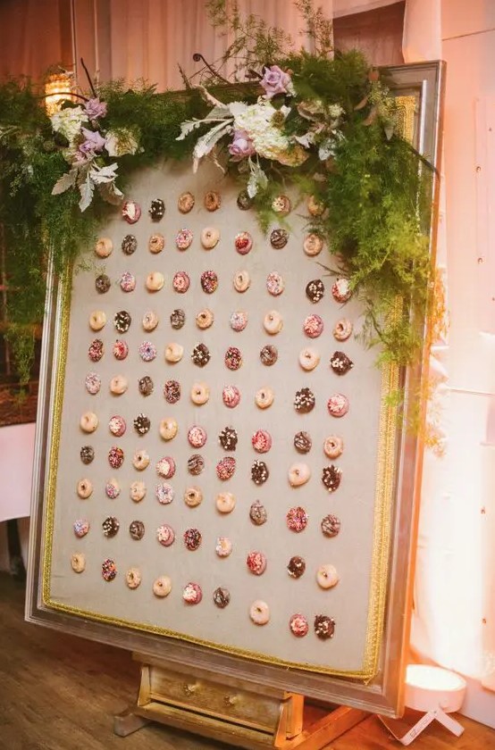 a chic framed donut wall with lush greenery and blooms looks liek a tasty artwork