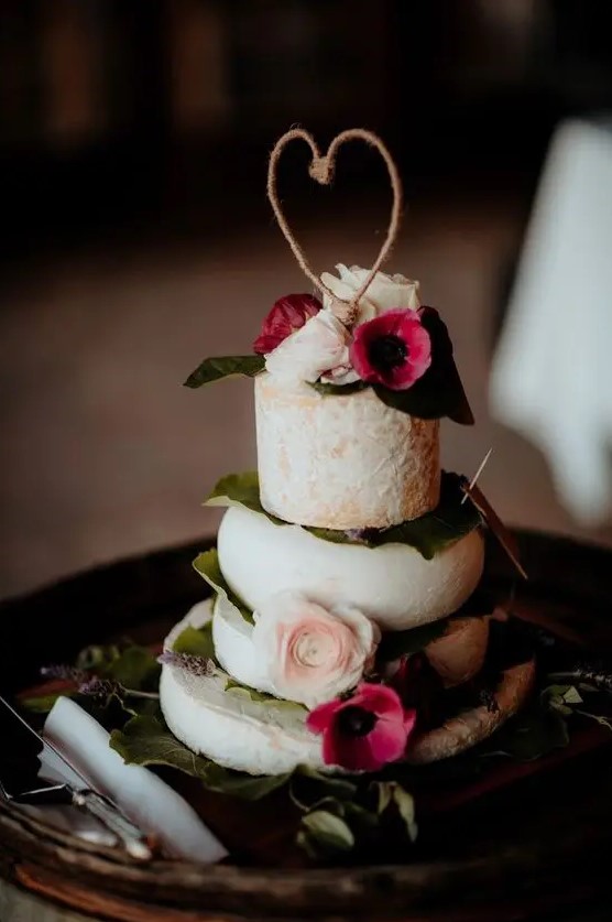 a lovely cheese stack wedding cake with foliage, blush and bold pink blooms plus a yarn heart topper is amazing for your wedding
