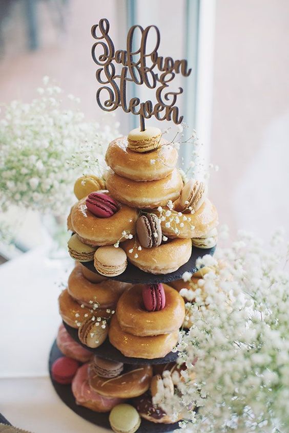 a lovely stand with glazed donuts and macarons, with baby's breath and a calligraphy topper is a cool alternative to a wedding cake