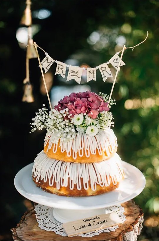 a relaxed two-tier bundt wedding cake with creamy drip, baby's breath and mauve hydrangeas and a banner topper