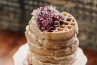 a small yet lovely waffle wedding cake with cream and some raspberries and pink blooms on top is amazing