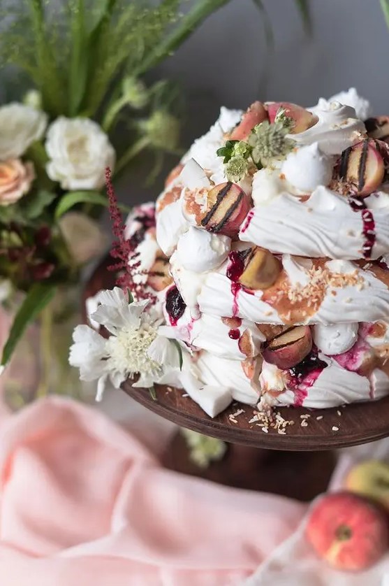 a summer-inspired pavlova wedding cake topped with fresh peaches, with cherry drip, neutral blooms is a veyr mouth-watering idea