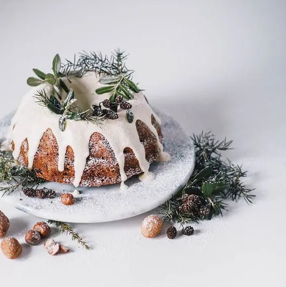 a traditional bundt wedding cake with white chocolate dripping, evergreens, pinecones and sugar powder to imitate snow