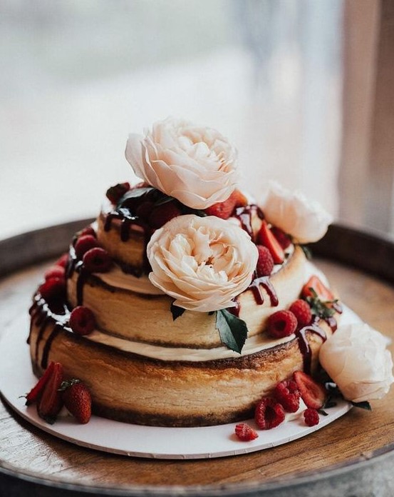 a two-stacked cheesecake topped with flowers and berries looks cute and absolutely delicious and adorable