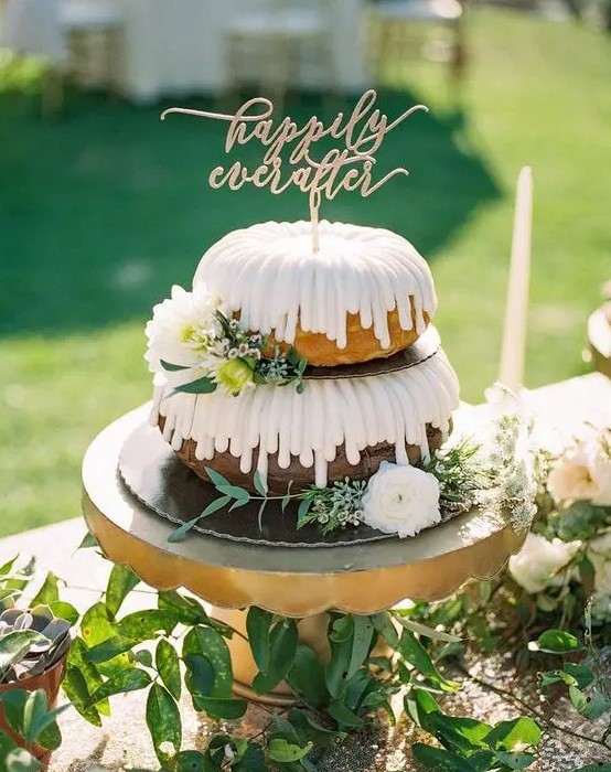 a two-tier bundt wedding cake with creamy drip, white blooms and greenery and a gold calligraphy topper