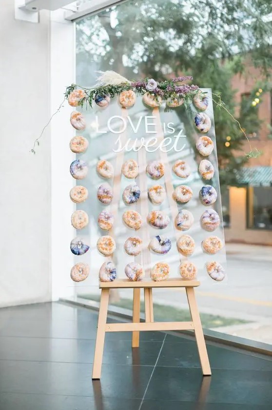a wedding donut wall with purple marble donuts, with purple blooms and greenery is a super trendy and edgy idea