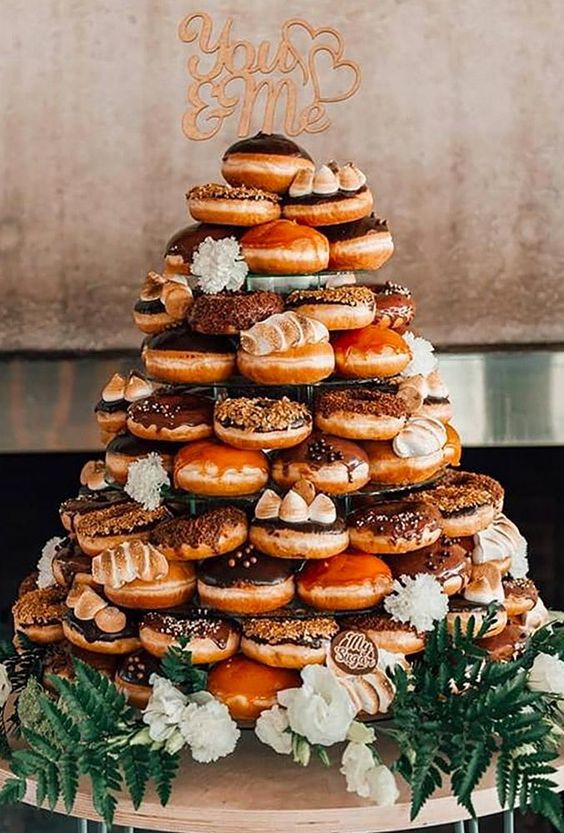 a whole tower of delicious caramel and chocolate donuts with a calligraphy topper and white blooms is wow