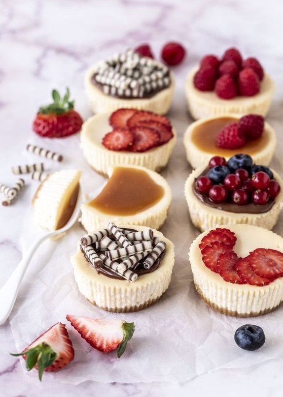 an assortment of mini cheesecakes with fresh berries and berry slices, salted caramel and mini chocolate bites