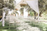 04 The wedding ceremony space was done with white curtains, white petals,sheer chairs and beautiful olive trees