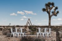 07 The wedding ceremony space was done with metal chairs, a triangle wedding arch with lush greenery and blooms