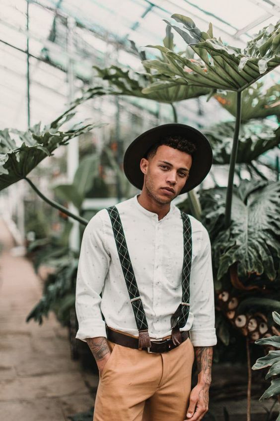 a boho groom's outfit with a printed shirt, beige pants, green printed suspenders and a black hat is a lovely idea