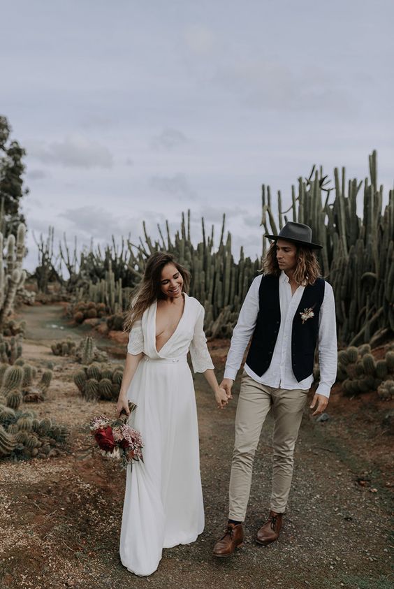 a boho groom's outfit with a white shirt, grey pants, brown shoes, a black waistcoat and a grey hat is a cool and pretty idea
