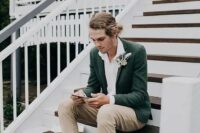 a casual and cool groom’s outfit with a white shirt, neutral jeans, a green blazer, brown shoes and blue socks plus a boutonniere