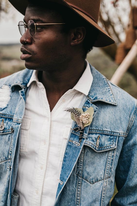 a cool relaxed groom's outfit with a white shirt, a blue denim jacket with a boutonniere and a brown hat is great for the fall