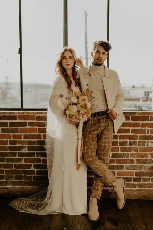 A creamy turtleneck, a creamy jacket, rust colored windowpane pants, tan Chelsea boots are a great look for a boho wedding