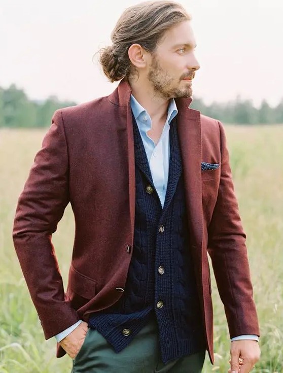 a fall or winter boho groom look with a blue shirt, a navy cardigan, a burgundy blazer, green pants and a braided man bun
