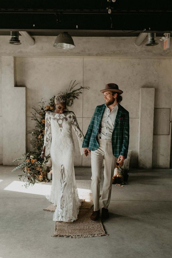 a lovely boho groom's look with a printed shirt, grey pants, a teal windowpane blazer, brown shoes and a tan hat
