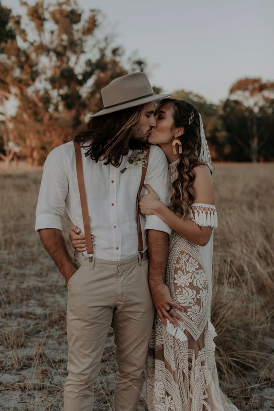 a lovely boho groom's outfit with a white shirt, grey pants, amber leather suspenders and a grey hat is a cool idea for a wedding