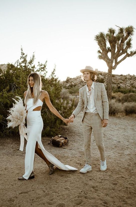 a neutral boho groom's look with a grey windowpane suit, a white shirt, white trainers and a hat is great for a desert wedding