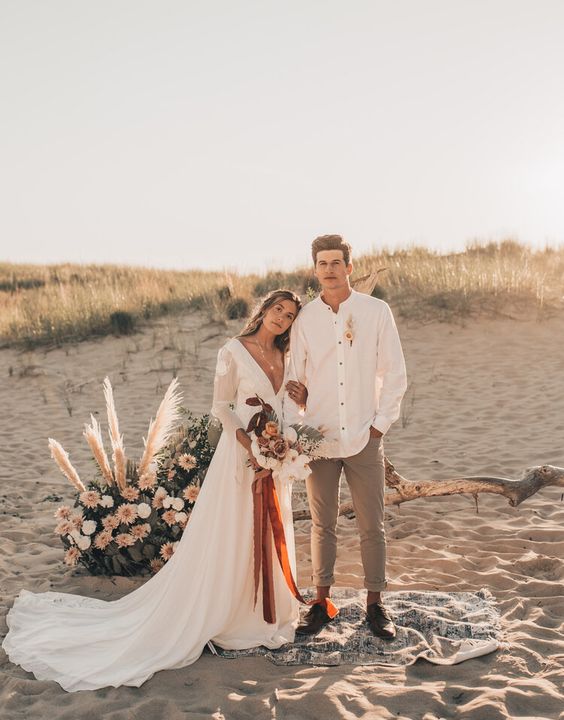 a pretty boho groom's look with an oversized white shirt, grey pants, black shoes and a boutonniere is a cool and easy to repeat outfit