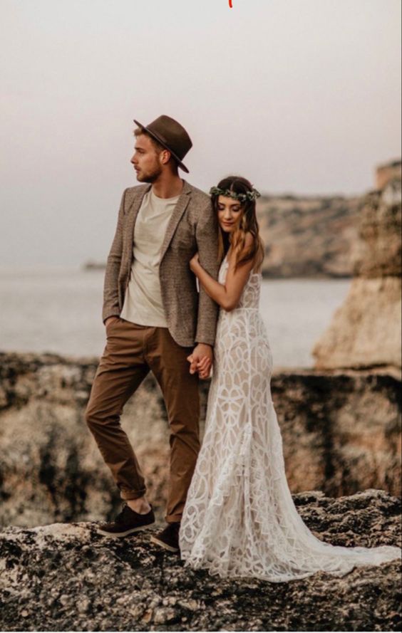 A relaxed groom's outfit with a neutral t shirt, rust colored pants, a grey blazer and a brown hat plus black shoes is cool for a boho wedding