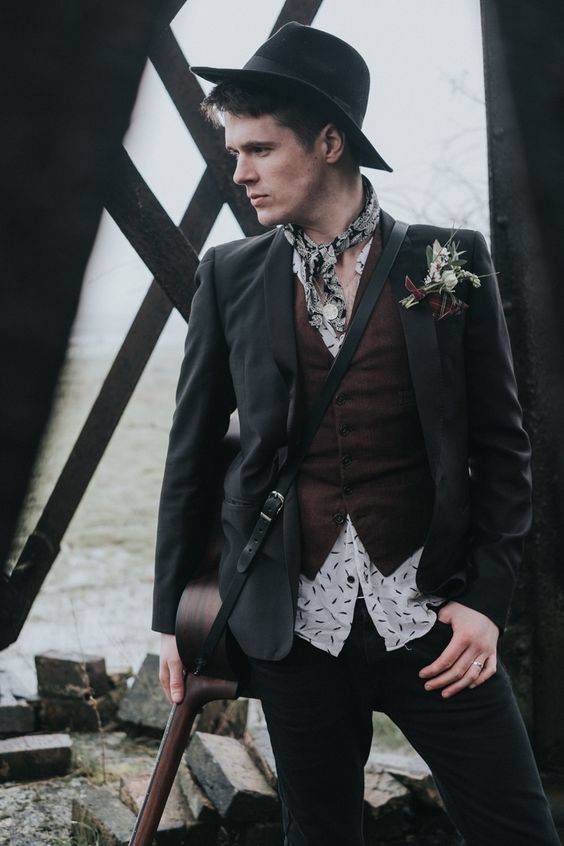 an alternative groom's look with a printed shirt, a brown waistcoat, a black blazer, a neck tie, a black hat and a boutonniere