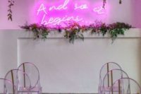 03 a chic modern wedding ceremony space with a pink neon sign, greenery, hanging blooms and acrylic chairs