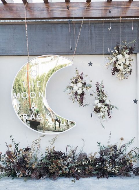 a beautiful wedding backdrop with a shiny silver moon, lush florals and dark and dried herbs and leaves