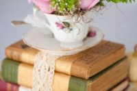 10 a stack of vintage books with a lace tie, a teacup with pink roses and greenery for a wedding centerpiece