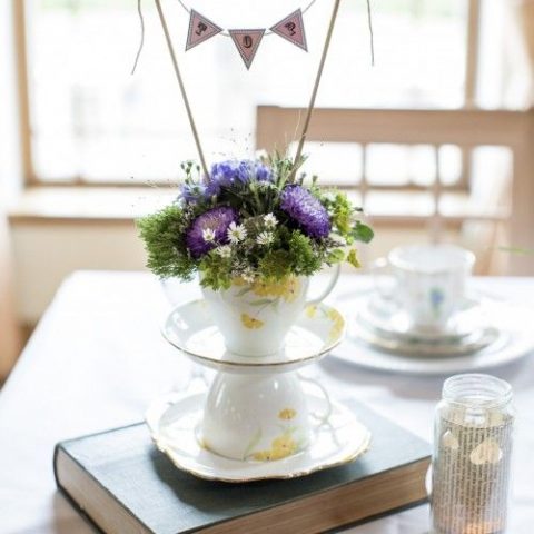 an elegant and whimsy wedding centerpiece with teacups, bright blooms and a banner on top