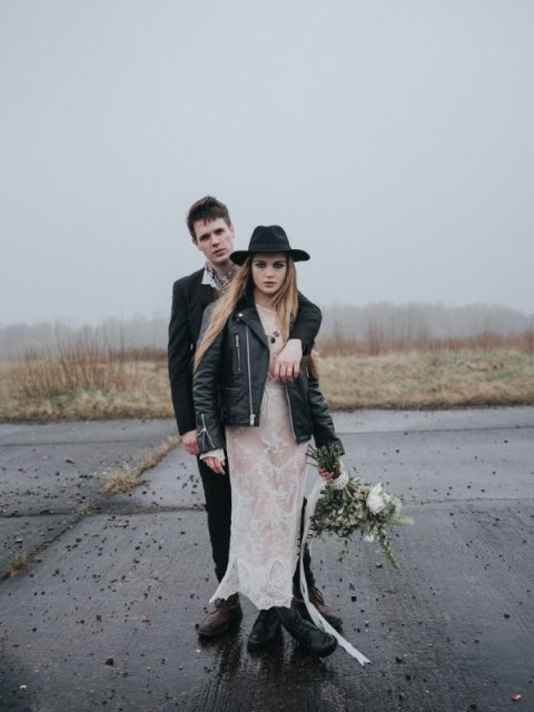a naked lace wedding dress, a black leather jacket, black boots and a black hat