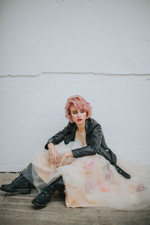 a romantic floral wedding dress with tall black boots, a black leather jacket and pink hair for a touch of rock